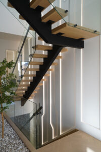 Modern floating staircase Toronto with wood treads, glass railing, and integrated vertical lighting